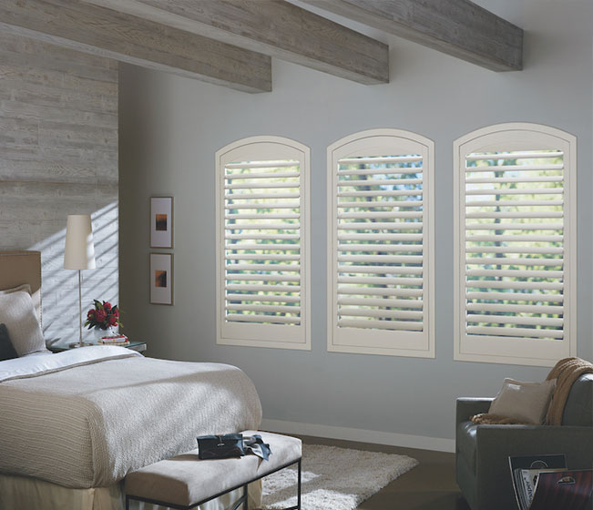 A bedroom with white shutters on the windows.